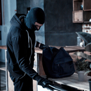 A burglar in a balaclava putting items into a bag.