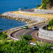 Winding coastal road with cars along rocky shoreline.