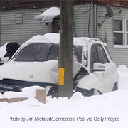 A white car dented after hitting a utility pole during a snowstorm