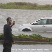 A man takes pictures with a cell phone near a car stuck in Windstorm Amy floodwaters in Ireland.