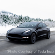A black Tesla sedan on a road with snow and trees in the background