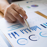 Hand pointing at financial charts on a paper.