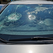 The windshield of a gray car shattered by hailstones