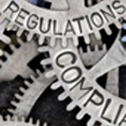 Macro photo of tooth wheel mechanism with the words regulation and compliance engraved on the wheels.