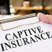 A hand holds a clipboard with a paper printed with "CAPTIVE INSURANCE"