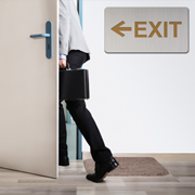 A man wearing a white shirt and black pants walking out a door marked 'exit'