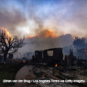 Rubble of a house destroyed in Palisades wildfires with flames and smoke in the background
